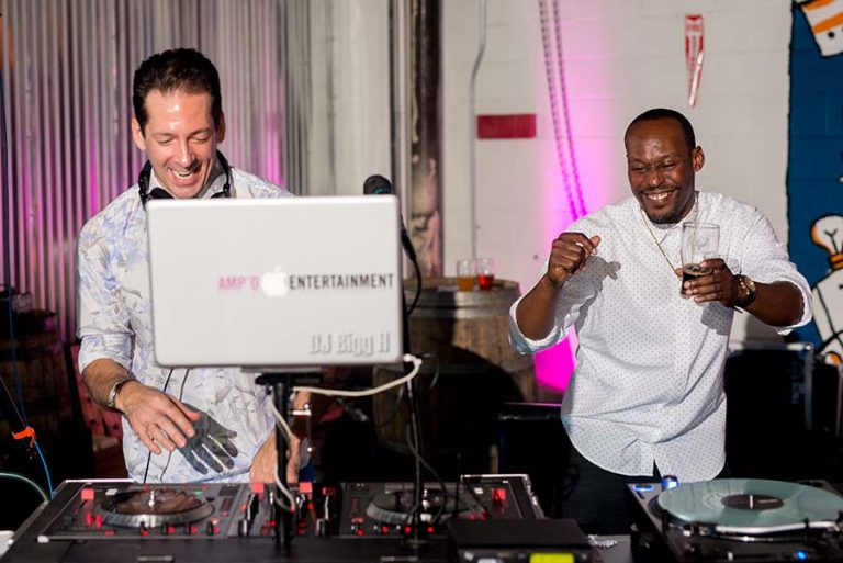 Two professional DJs performing together at wedding reception with pink ambient lighting