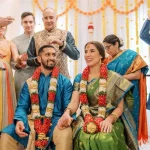 Bride and groom in traditional Indian wedding attire seated during ceremony with family showering them with flower petals
