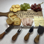 Personalized Arellano charcuterie board with grapes, crackers, cheese, and meat alongside cheese knives