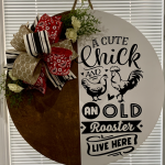 Circular door hanger with "A Cute Chick and an Old Rooster Live Here" text, decorated with red bandana bow and cream flowers