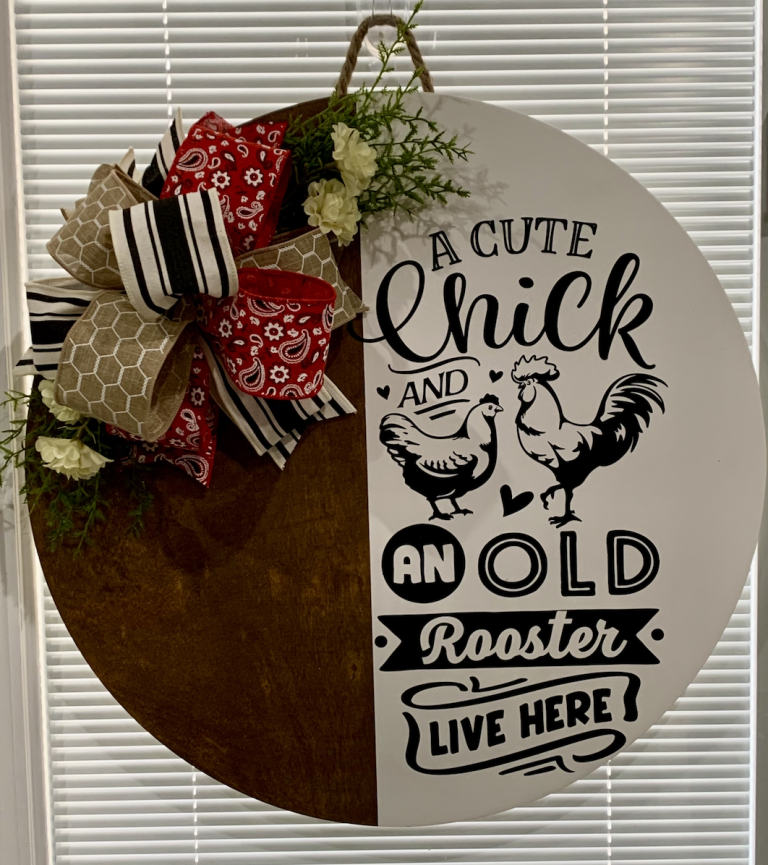 Circular door hanger with "A Cute Chick and an Old Rooster Live Here" text, decorated with red bandana bow and cream flowers