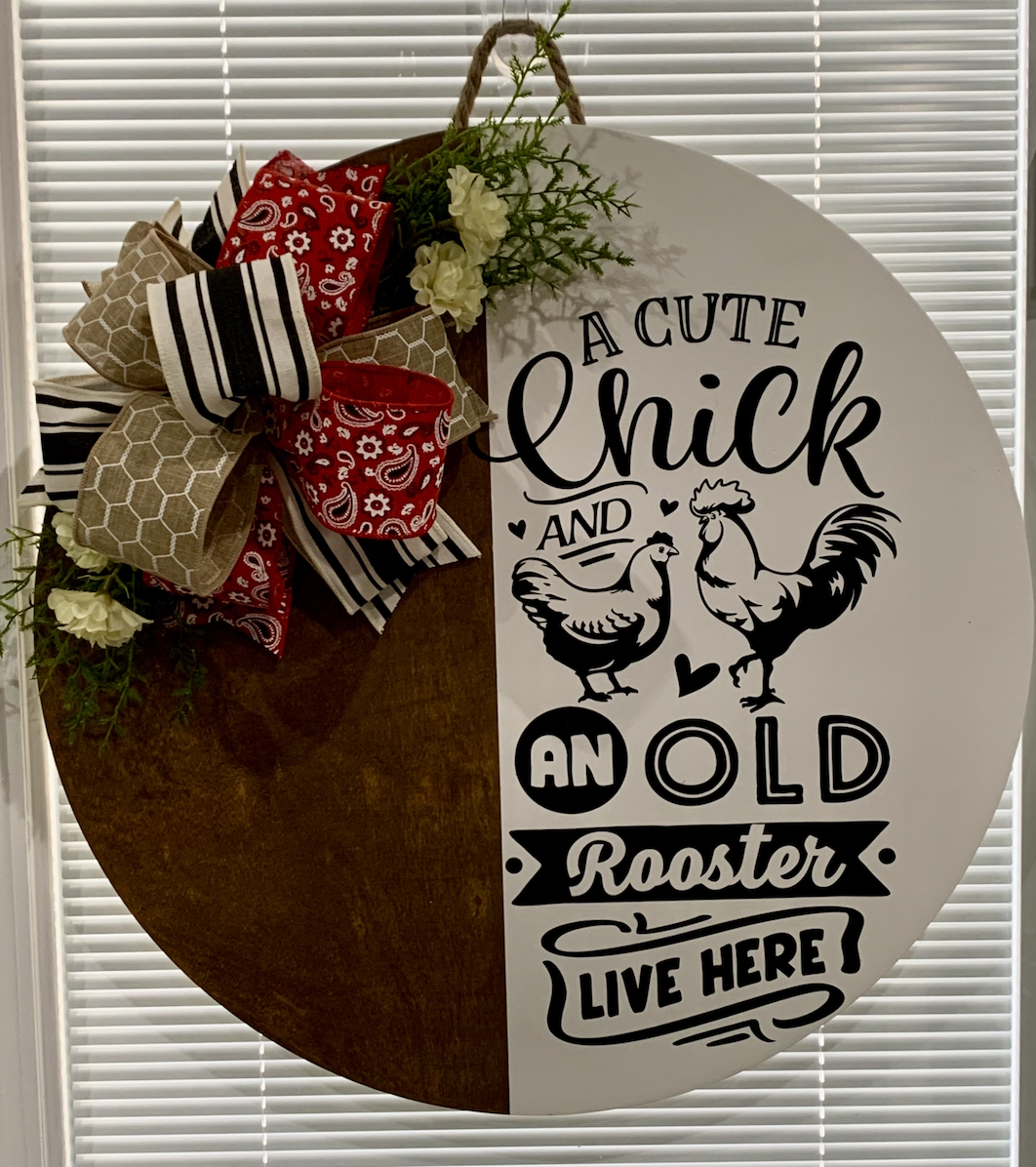 Circular door hanger with "A Cute Chick and an Old Rooster Live Here" text, decorated with red bandana bow and cream flowers