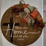 Rustic wooden wreath with fall foliage, plaid ribbon, and "Bless this home and all who enter" text