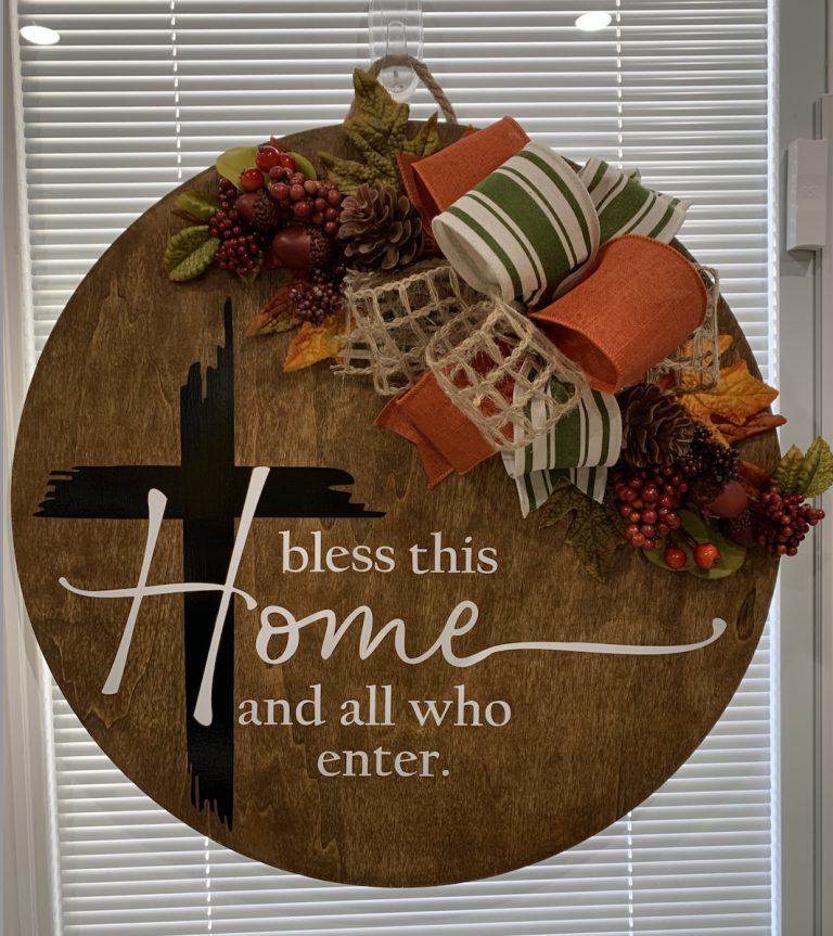Rustic wooden wreath with fall foliage, plaid ribbon, and "Bless this home and all who enter" text
