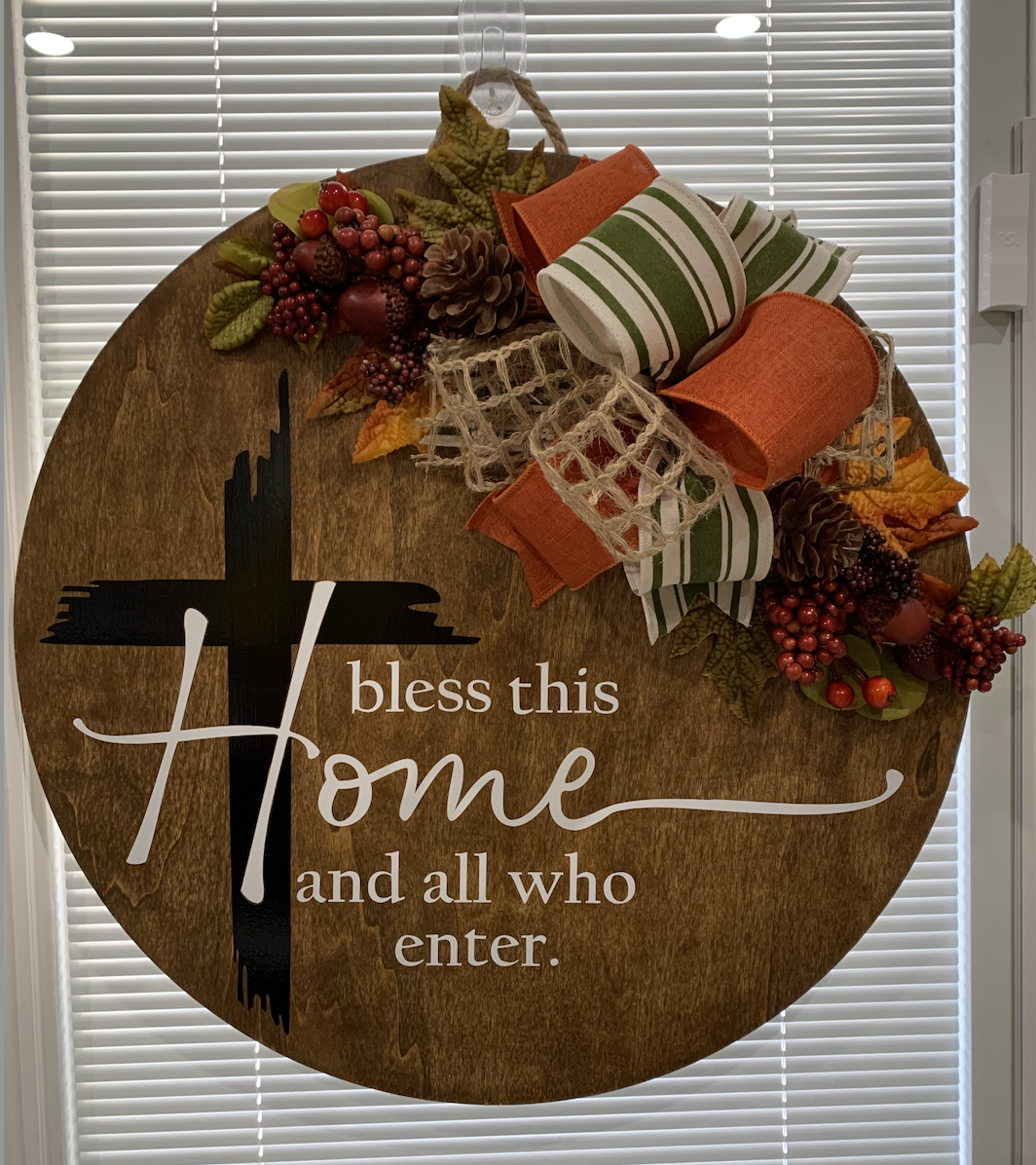 Rustic wooden wreath with fall foliage, plaid ribbon, and "Bless this home and all who enter" text