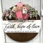 Round wooden door hanger with pink and floral ribbons, eucalyptus leaves, and "Faith, hope & love" biblical quote