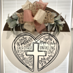 White round door hanger with heart-shaped cross design featuring 1 Corinthians 13 love verses, topped with pink and gold ribbons