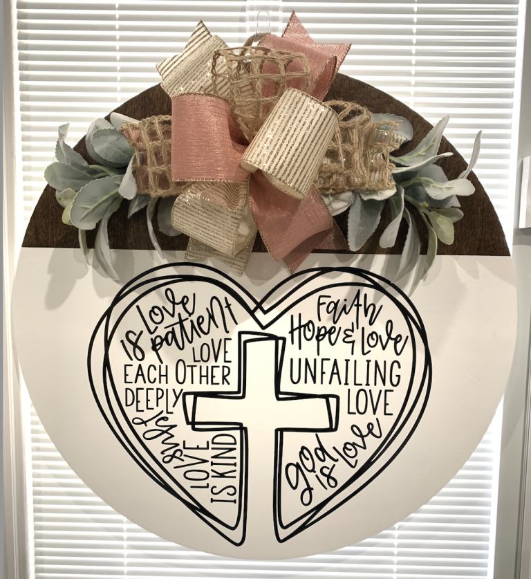 White round door hanger with heart-shaped cross design featuring 1 Corinthians 13 love verses, topped with pink and gold ribbons