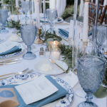 Wedding tablescape featuring blue glassware, white taper candles, and blue floral china place settings