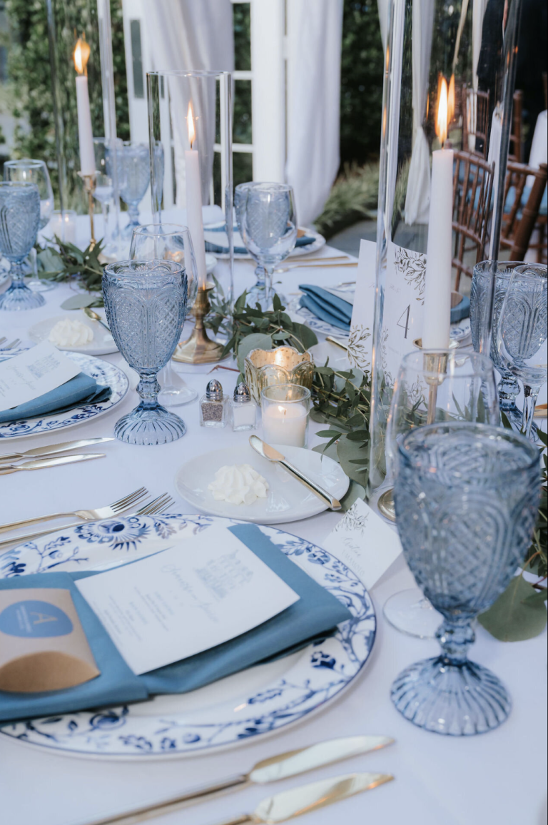 Wedding tablescape featuring blue glassware, white taper candles, and blue floral china place settings
