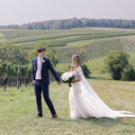 Bride and groom holding hands in front of rolling vineyard landscape in Northern Virginia