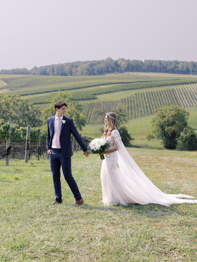 Bride and groom holding hands in front of rolling vineyard landscape in Northern Virginia