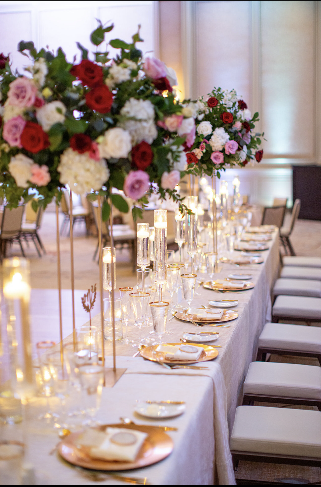 Elegant wedding reception table with tall rose centerpieces, gold-rimmed place settings, and pillar candles