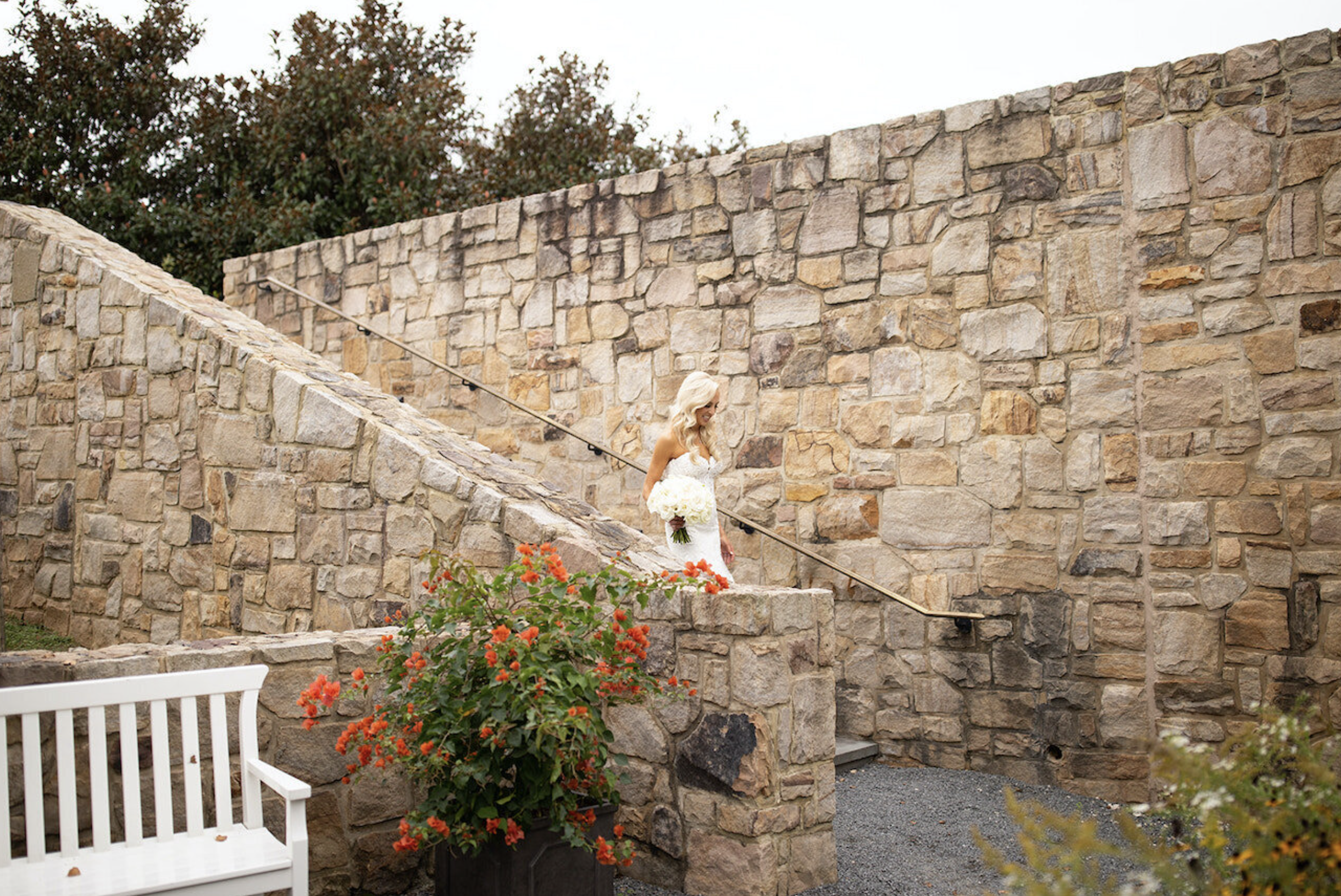 Outdoor stone staircase with metal railings, white bench, and flowering plants