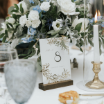 Wedding table centerpiece with white roses, blue flowers, table number 8 card, and lit candles