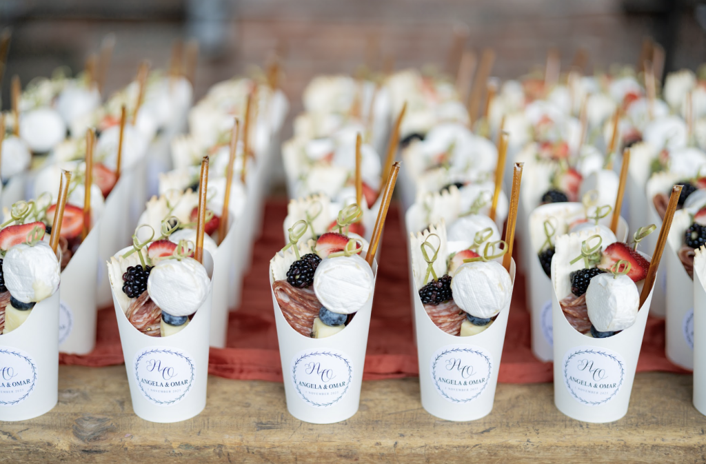 Personalized charcuterie cups topped with berries and prosciutto arranged on wooden table