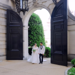 Couple walking through arched stone entrance of historic building with manicured greenery