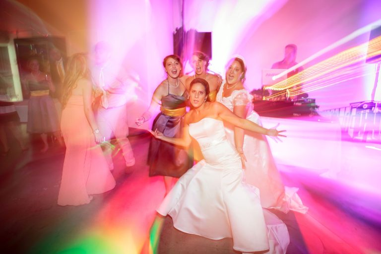 Bride and bridesmaids dancing together under colorful uplighting at wedding reception