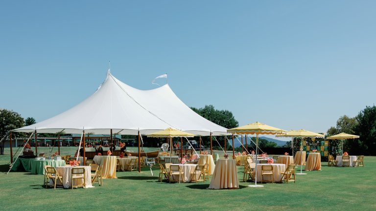 Outdoor wedding reception tent with rustic decor overlooking green lawn on sunny day