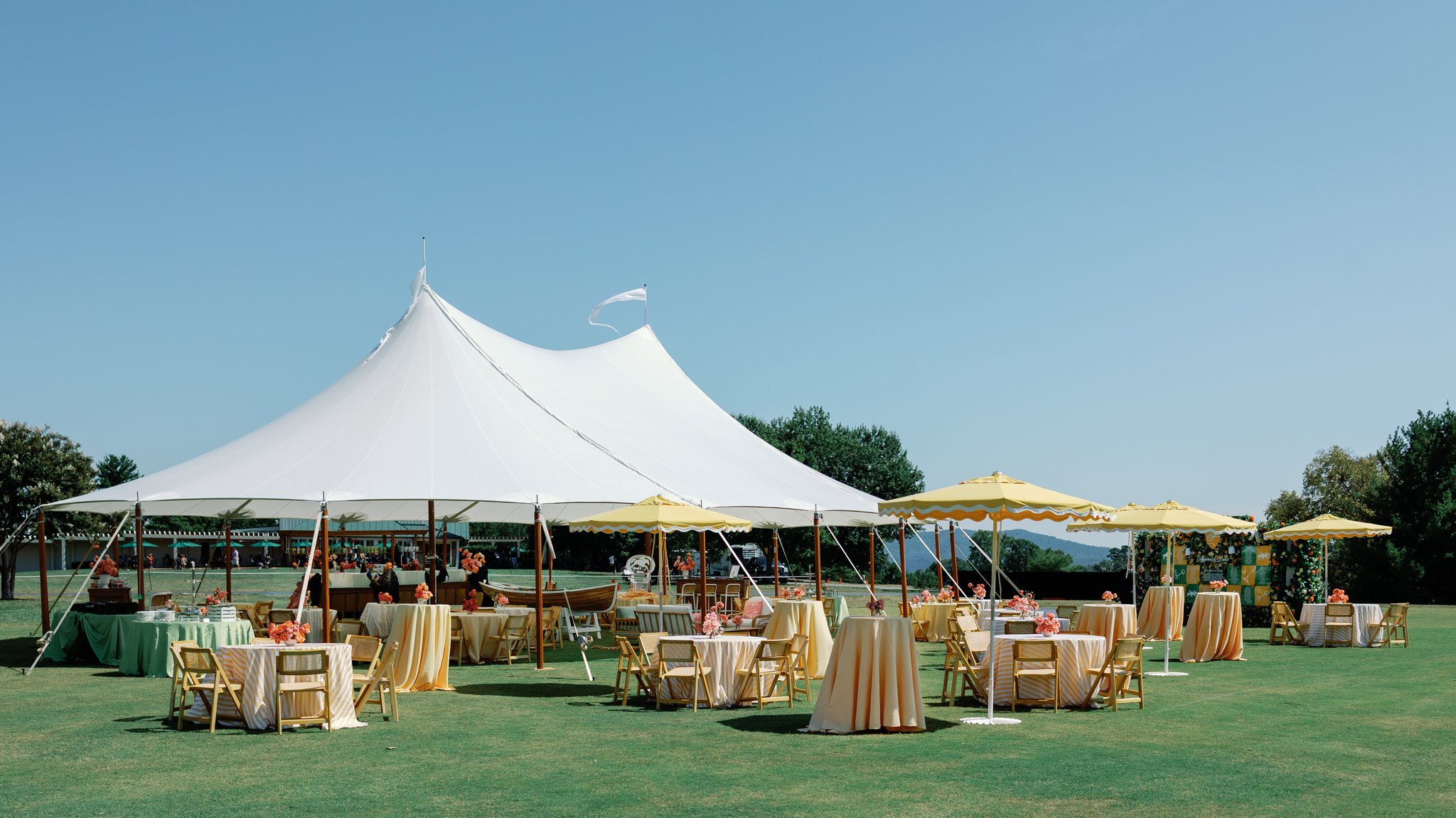 Outdoor wedding reception tent with rustic decor overlooking green lawn on sunny day