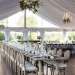 Elegant tented wedding reception with long banquet tables, crystal chandeliers, and greenery centerpieces