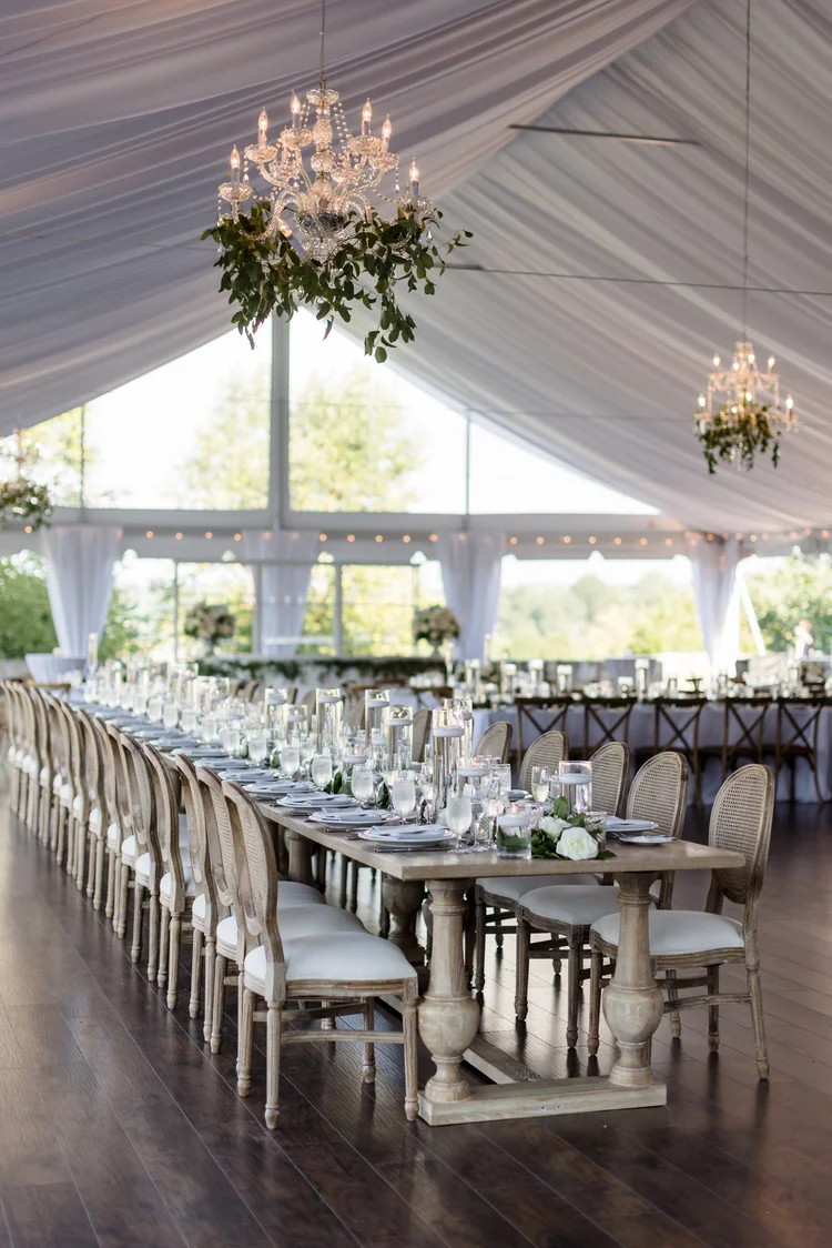 Elegant tented wedding reception with long banquet tables, crystal chandeliers, and greenery centerpieces
