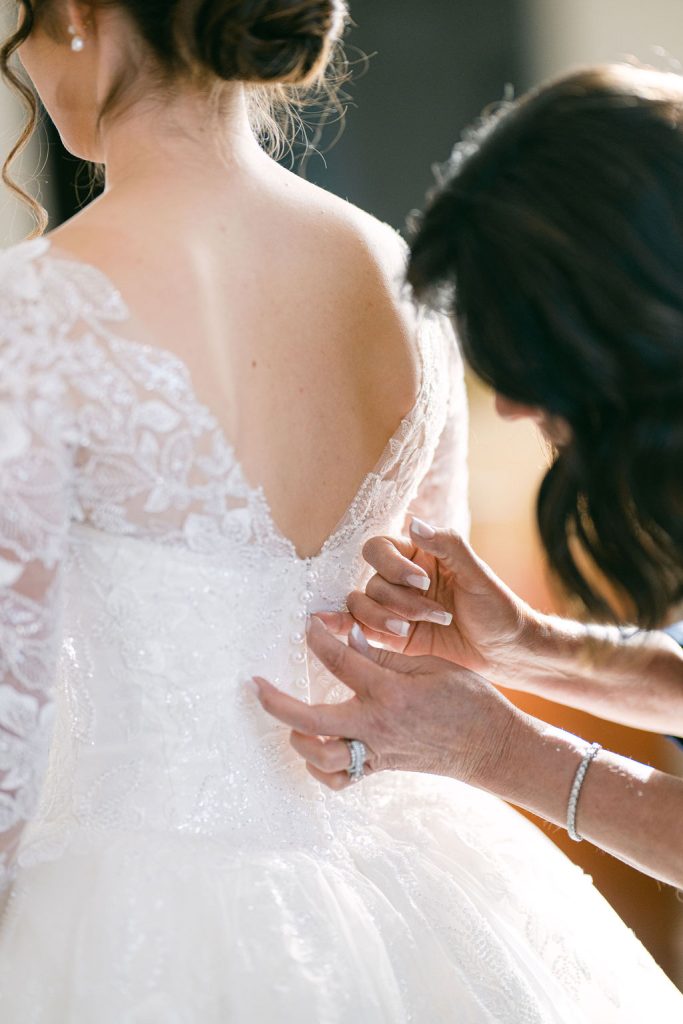 Bride being helped into her lace wedding gown with delicate back detailing