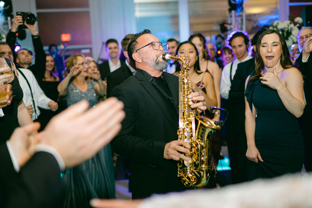 Saxophonist performs surrounded by dancing wedding guests at Victoria and Anthony's celebration