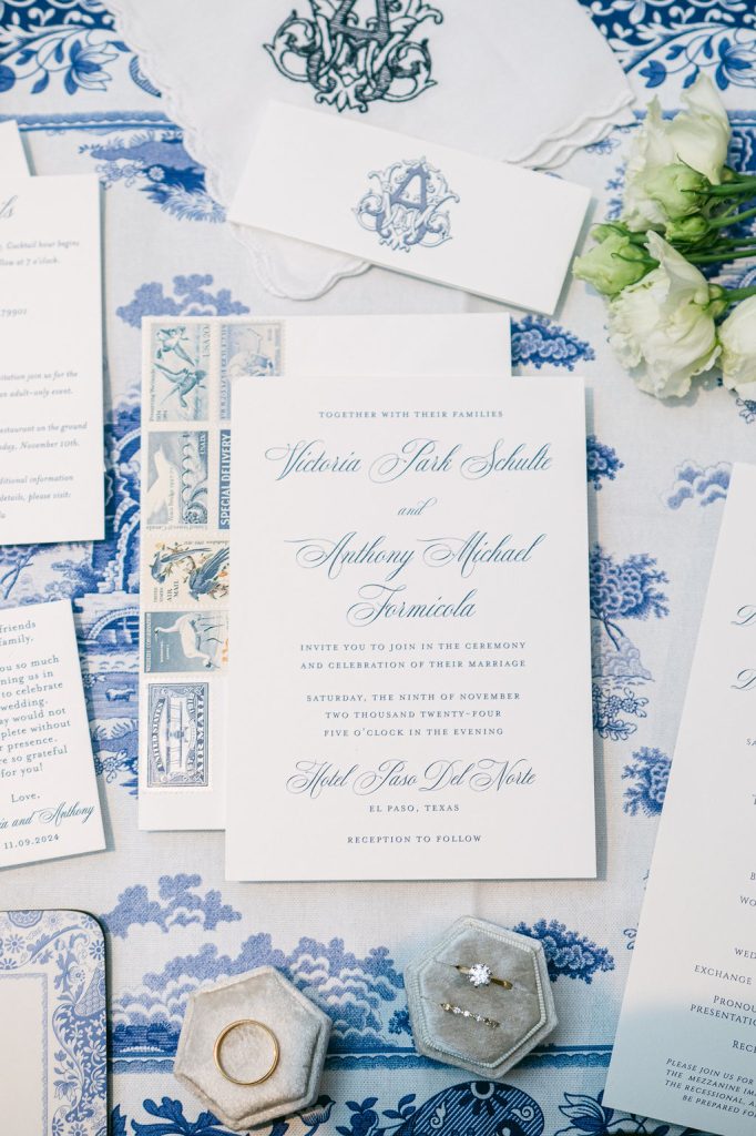 Wedding invitation suite in blue and white featuring Victoria and Anthony's names, with monogrammed envelope, vintage stamps, and rings in hexagonal boxes