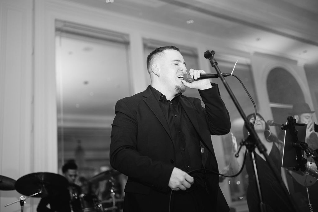 Male vocalist in black suit performs with microphone at wedding reception