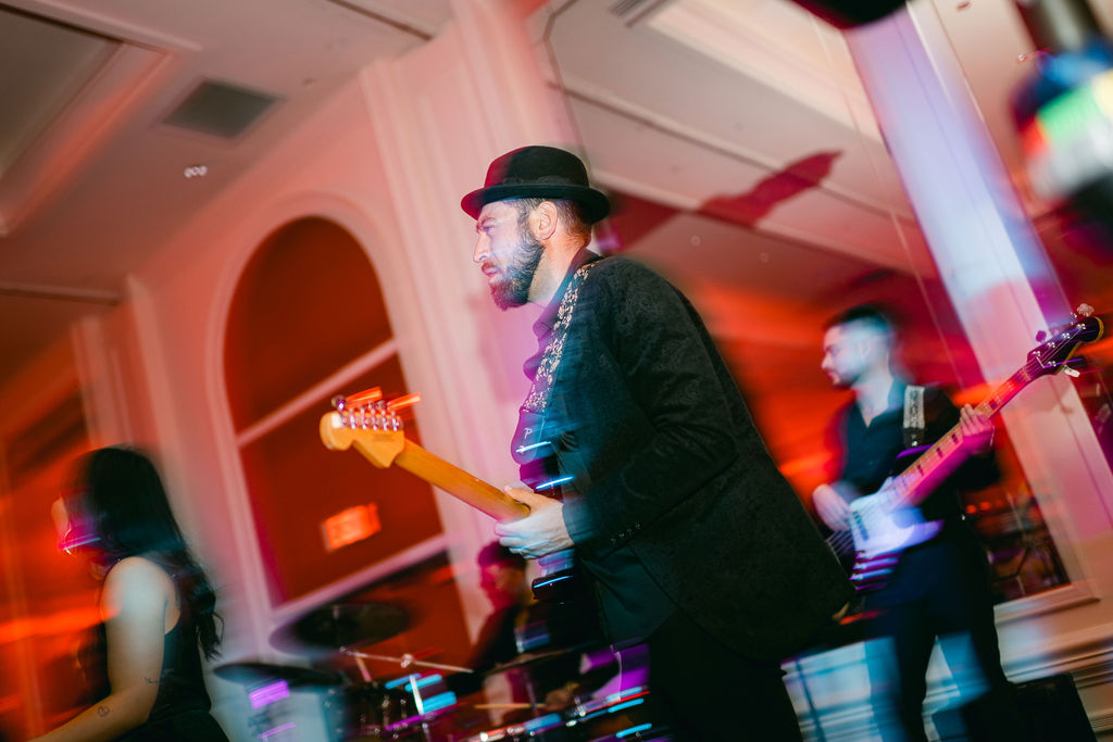 Live band guitarist performing in fedora hat with colorful stage lighting at wedding reception