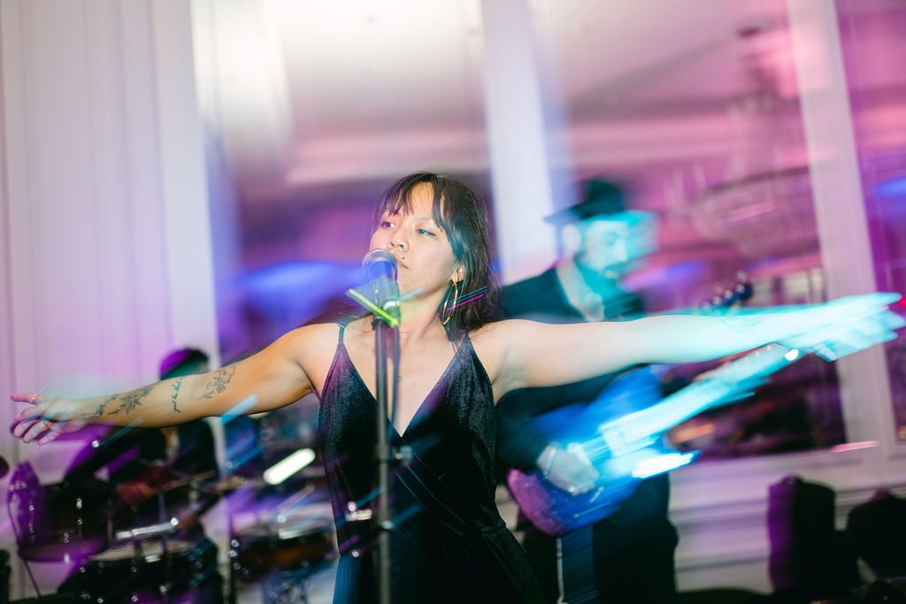 Female singer performing with outstretched arms under purple and blue lighting at Victoria and Anthony's wedding reception