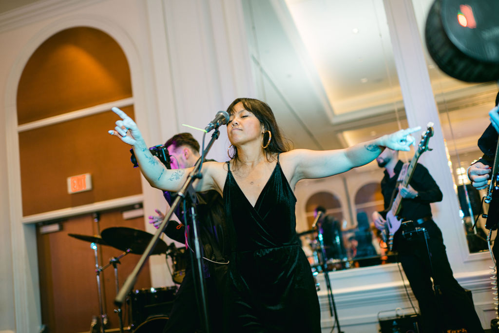 Female singer in green velvet dress performs with arms outstretched at wedding reception