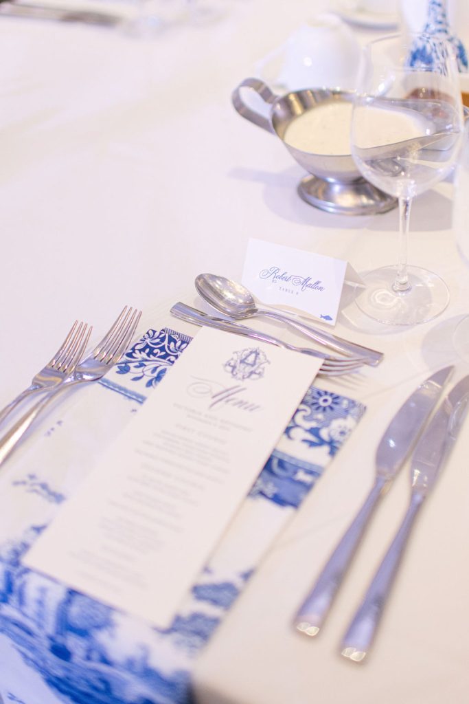 Elegant place setting with blue and white patterned menu card, silverware, and wine glass