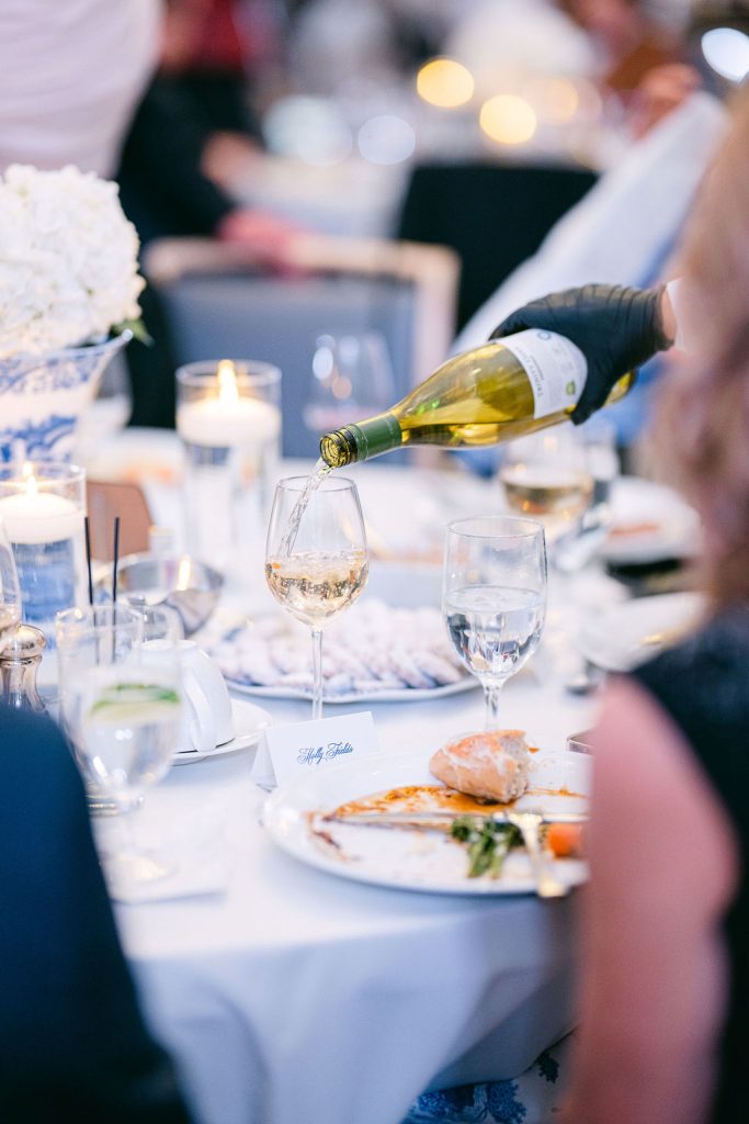 White wine being poured into stemware at an elegant reception table with dinner service and candles