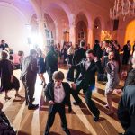 Wedding guests dancing on illuminated ballroom floor with warm amber uplighting and elegant chandelier