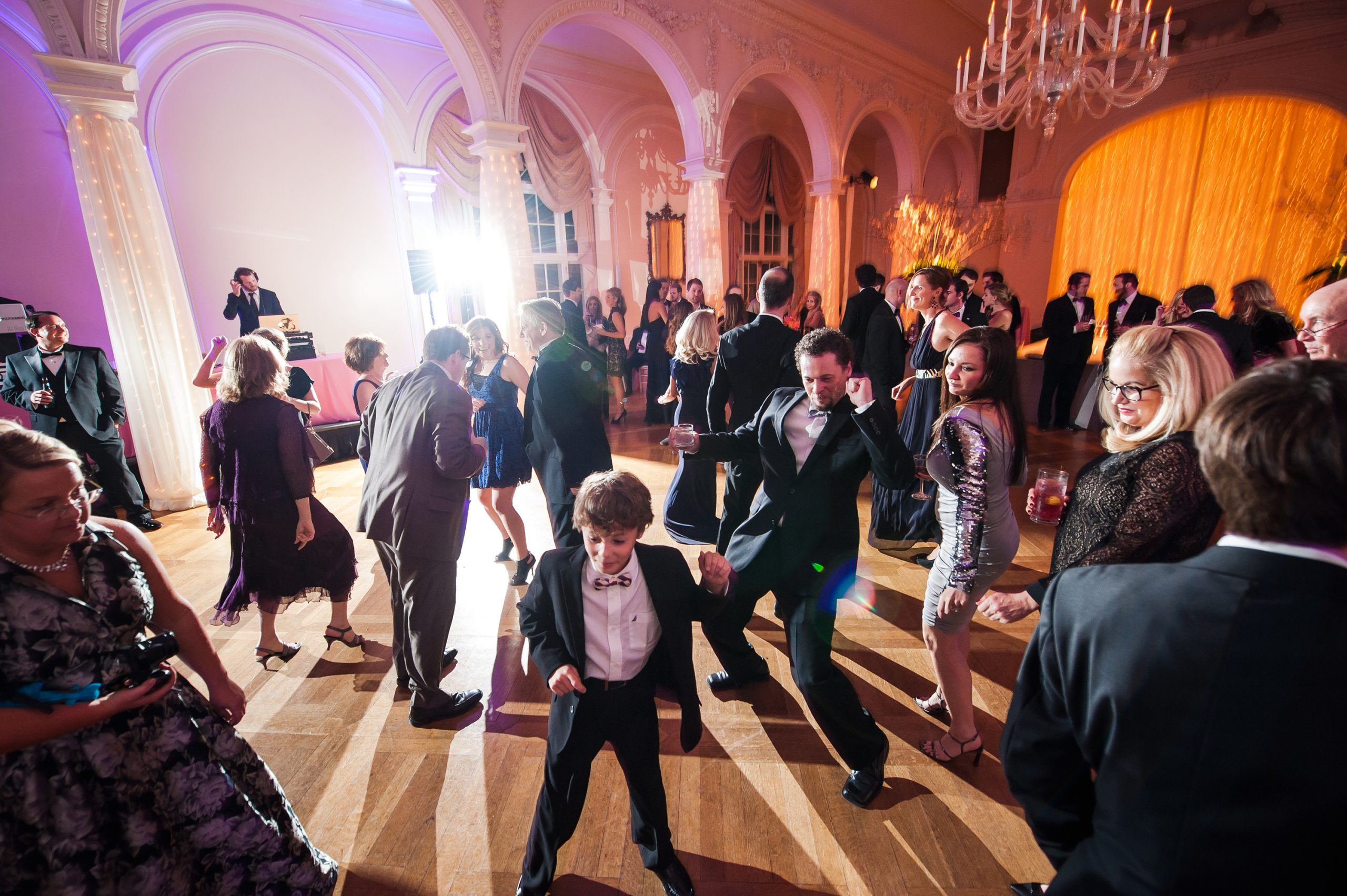Wedding guests dancing on illuminated ballroom floor with warm amber uplighting and elegant chandelier