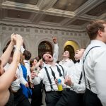 Wedding guests dancing and celebrating energetically in an elegant ballroom with ornate ceiling and arched windows