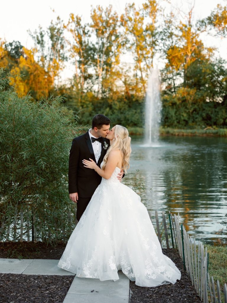Newlyweds kissing by fountain and fall foliage at outdoor wedding venue