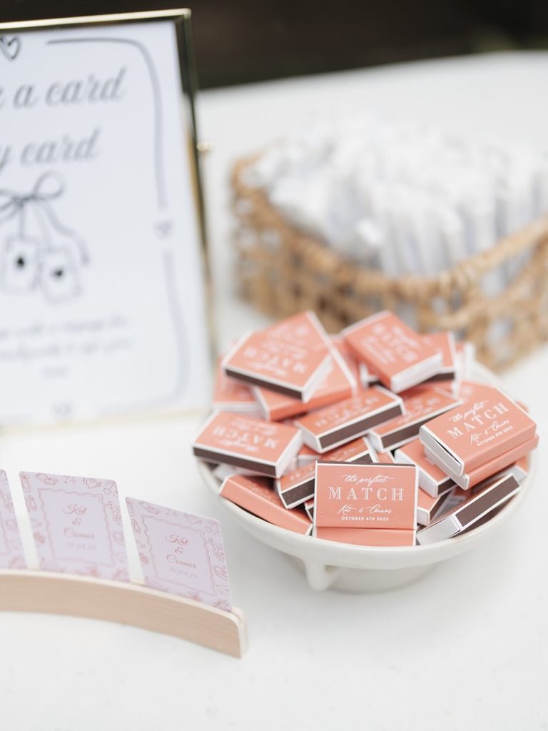Coral matchbooks personalized with couple's names displayed in white dish with wedding signage