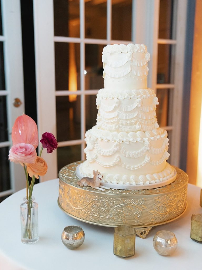 Four-tier white wedding cake with ornate piping on vintage gold stand