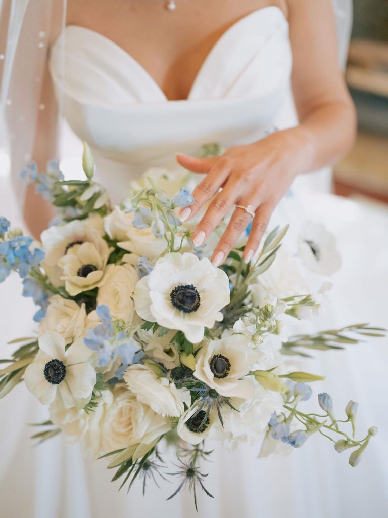Bride holding white and blue bridal bouquet with engagement ring visible