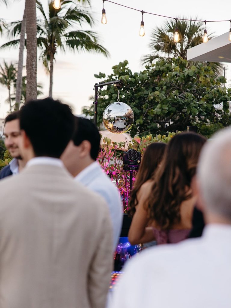 Outdoor tropical reception with disco ball and string lights among palm trees