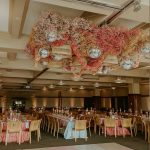 Grand ballroom featuring dramatic hanging floral installation with disco balls above tables set with coral linens