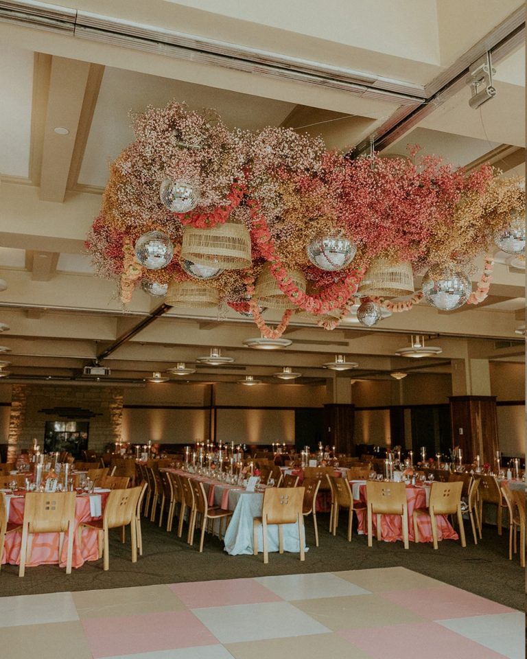 Grand ballroom featuring dramatic hanging floral installation with disco balls above tables set with coral linens