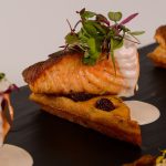 Pan-seared salmon on crispy waffle with cherries, cream sauce, and microgreens