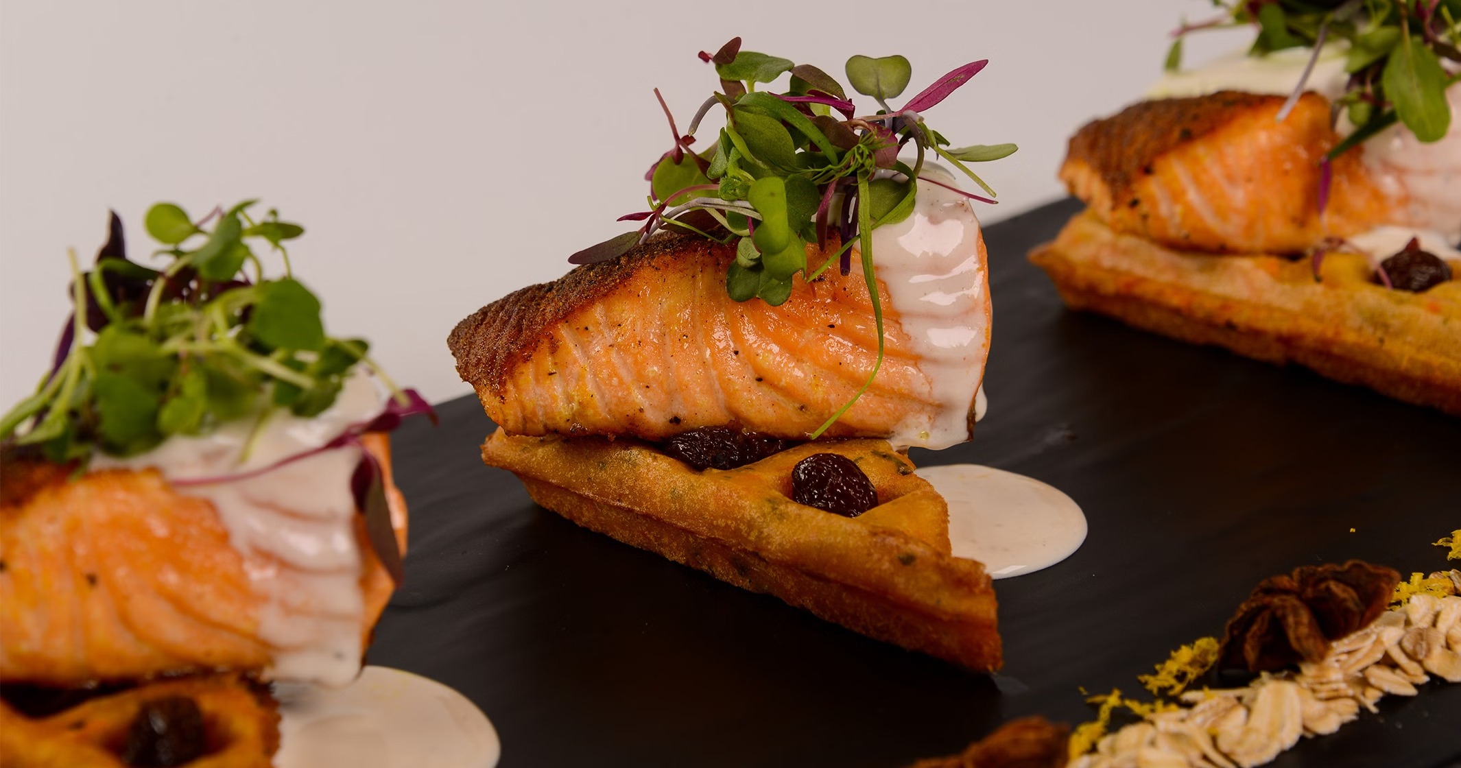 Pan-seared salmon on crispy waffle with cherries, cream sauce, and microgreens
