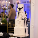 Four-tier white wedding cake with textured fondant details and elegant black ribbon bows at an Alpharetta reception
