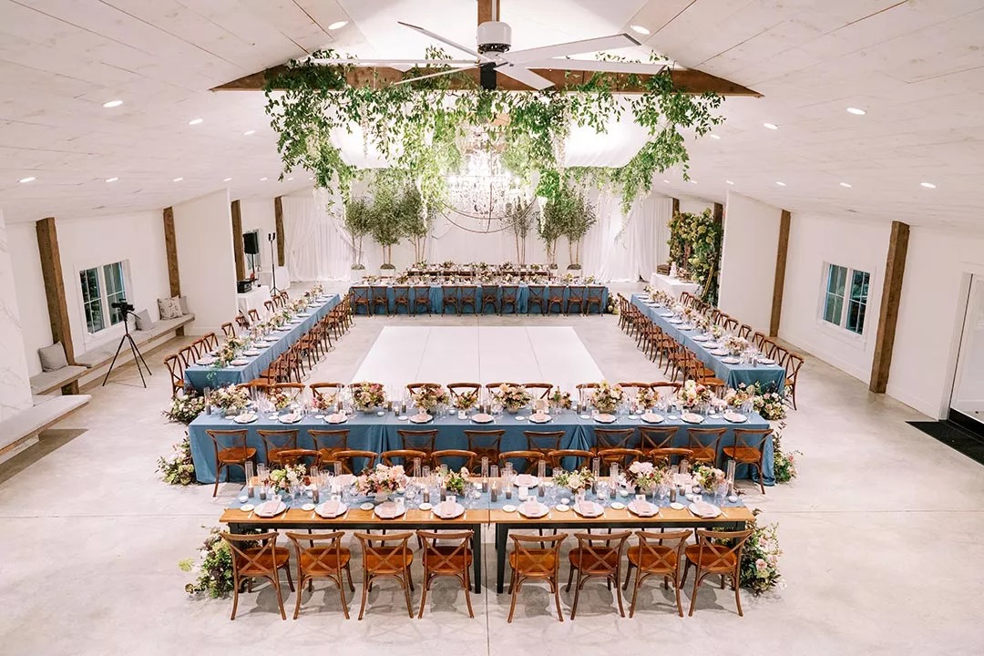 Indoor wedding reception with square layout and dance floor in middle with greenery above