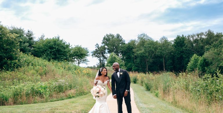 Bride and groom walking together on tree-lined path through natural field at Salamander Resort